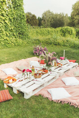 Summer picnic outdoor in the garden on green grass in Boho style. Tasty snacks, fresh fruits and cold drinks. Food and drink concept