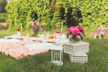Beautiful summer celebration picnic in green garden making by event agency. Flowers decorations with peonies. Floristic. Leisure and fun. Tasty food and drinks outdoors. Selective focus