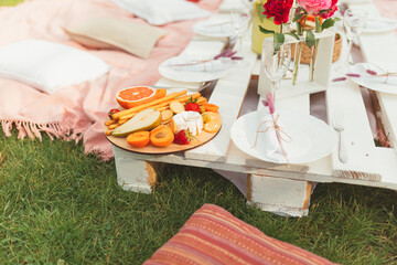 Summer picnic in the garden with tasty food and drinks. Focus on the plate with strawberries, apricots, pear, grapefruit, grissini and crackers. Celebratory serving. Selective focus. Leisure and rest