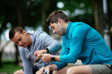 Fit young men taking rest from running. Two friends training outdoors.	