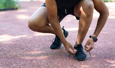 Closeup view of black jogger tying laces on his sports shoes during his training outside