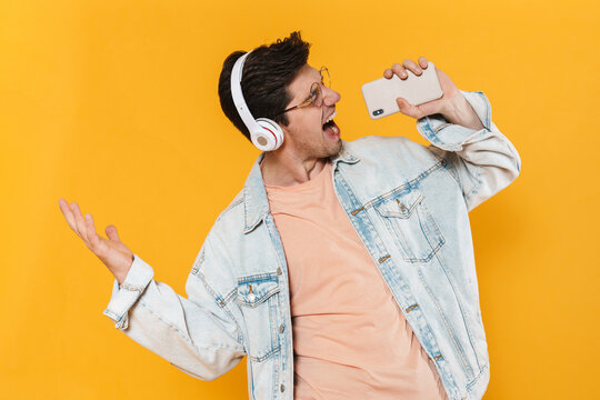 Photo of ecstatic man using mobile phone and headphones while singing