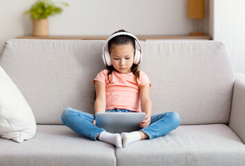 Girl Using Digital Tablet And Earphones Watching Cartoons Sitting Indoor