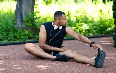 Black sportsman stretching on road at park after his morning run