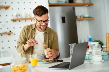 Young man eating breakfast and reading the news online. Handsome man enjoying at home.	