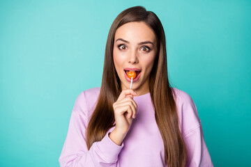 Photo of pretty funny lady hold lollipop hands good mood sweets addicted person lick bite tasty candy wear violet pullover isolated vibrant teal color background