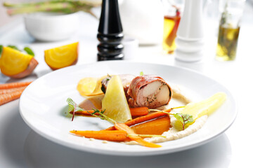 Rabbit roulade with prosciutto ham, celery puree and carrot glazed. A gourmet dish on a white plate. Food photography.