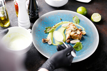 Grilled tuna steak with pistachio nuts, capers and green peas. Tasty dish on a blue plate. Food photography. The chef serves the dish.