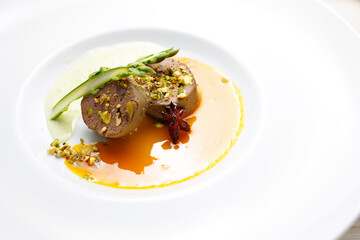 Goose terrine, roasted pistachios puree with asparagus served on an orange and anise sauce. A gourmet dish on a white plate. Food photography.