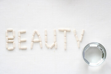 word BEAUTY made from collagen pills and glass of water on white textile background. Healthy lifestyle concept.