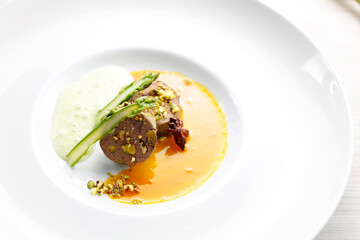 Goose terrine, roasted pistachios puree with asparagus served on an orange and anise sauce. A gourmet dish on a white plate. Food photography.