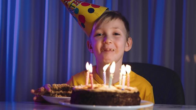 Cute boy eats cake on his birthday.  Happy child takes a piece of celebration cake and then bite it and swallow.  Happy white  boy celebrates his birthday. Caucasian cheerful child and birthday cake