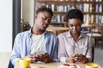 Fototapeta na wymiar Phubbing problem. Black couple stuck in their smartphones on boring date at cafe