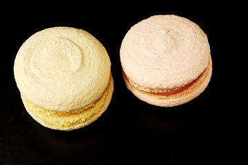 Two tasty macaroons on the black cafe table. Delicious candy and bakery. Food and drink backgrounds for restaurants