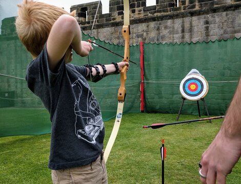 An unidentifiable young man shoots an arrow from a bow into a target at an archery range