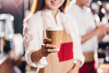 Asian Barista serving a paper cup of coffee to customer in coffee shop, Small business owner and startup in coffee shop and restaurant concept.