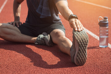 Runner man is stretching legs preparing for run training on track.