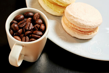 Plate with tasty macarons and coffee cup with raw coffee beans. Delicious baked food. Cafe and restaurant backgrounds