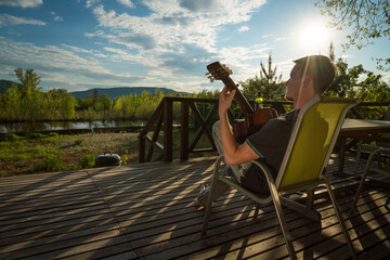 Young man playing guitar and drinking wine alone. Covid-19 quarantine.
