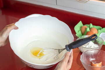 Eggs and milk in a bowl, a whisk and female hands.