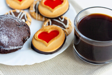 Breakfast, coffee in a glass cup, chocolate muffin and cookies with glaze on a white plate, napkin