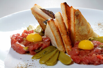 Steak tartare with toast and pickled cucumbers on a white plate