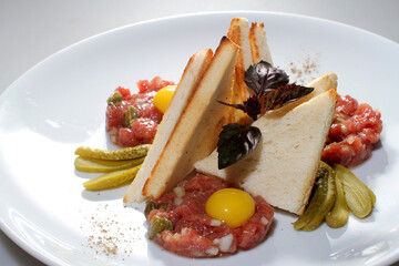 Steak tartare with toast and pickled cucumbers on a white plate