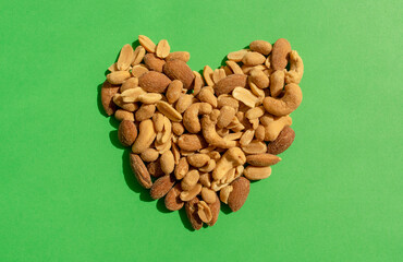 Various nuts forming heart shape on green background. Top view. Different kind of tasty and healthy nuts, snack.