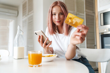 Photo of woman holding credit card and cellphone while having breakfast