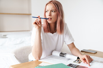 Image of perplexed caucasian woman doing homework with exercise books