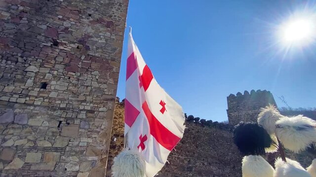 Papakha and georgian flag near ancient castle.