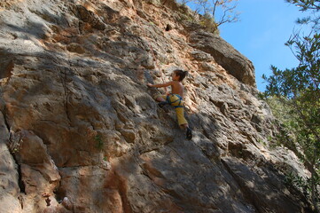 little boy climbs on the rock with rope