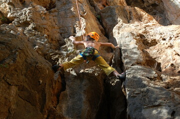 little boy climbs on the rock with rope