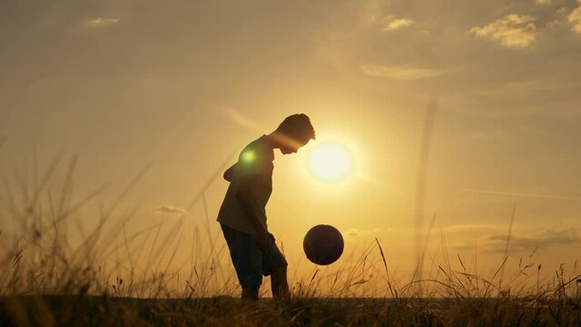 The path to the dream. The silhouette of a child chasing a ball with his foot at sunset. A boy plays soccer in the Park. Happy family. Active lifestyle of children. Sporting achievement