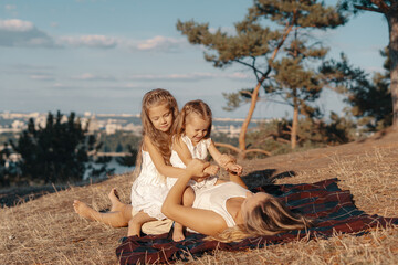 A beautiful young woman lying on blanket with her daughters. Happy family spends their day in the nature. Three blonde females, mother with her two little kids.