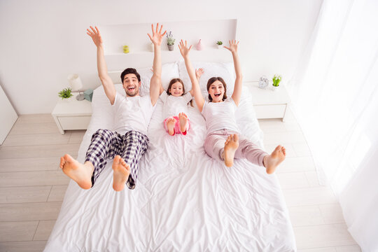 Photo of happy family barefoot mommy daddy daughter lying sheets good mood having fun spend together quarantine weekend raise arms legs self isolation offspring bedroom indoors