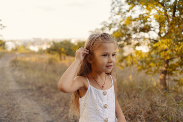 Naklejka premium Lovely carefree little girl wearing white clothes enjoy the day and sunshine rays while playing in the nature