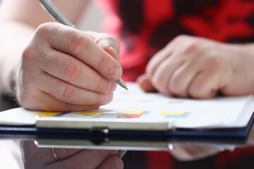 Close up of young man with pen in hand sitting at the table and making notes at work