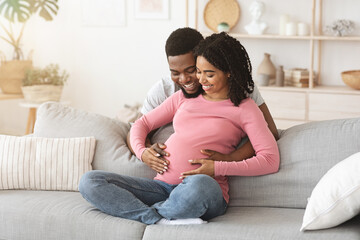 Positive young pregnant african couple embracing at home