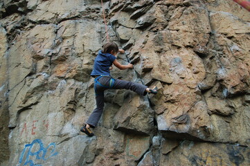 little boy climbs on the rock with rope