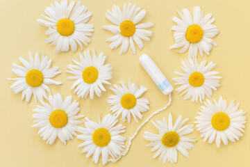 Hygienic female tampon with chamomile flowers on pastel yellow background. Women intimate hygiene in menstruation period and health care concept. Flat lay. Top view