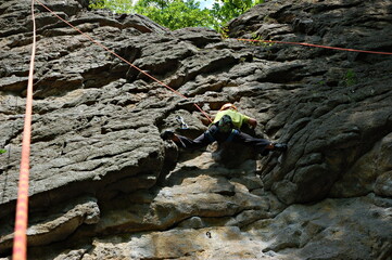 little boy climbs on the rock with rope