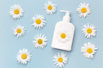 White cosmetic dispenser bottle of cream, gel or lotion with chamomile flowers extract on light blue background. Body skin and health care concept. Top view. Flat lay