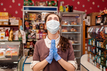 Small businesses during the pandemic. A female worker in a medical mask and rubber gloves, spreads her hands and looks up with hope. Concept of protection against coronavirus