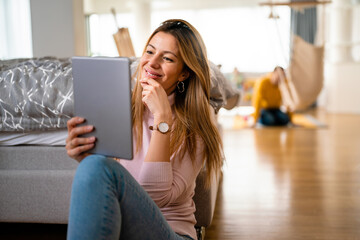 Beautiful young woman using digital tablet and smiling while sitting at home