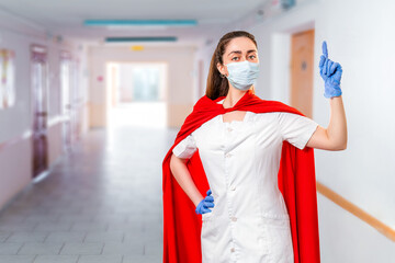 A doctor wearing medical face mask, gloves and a superhero Cape calls for protection from viruses. In the background a corridor of the hospital. The concept of the Power of a super hero for medicine © _KUBE_