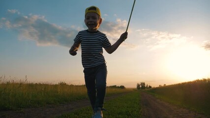 a happy child runs with a net on a sunset walk in the garden. Curious boy has fun outdoors, catching butterflies in the Park. Summer entertainment on a weekend.
