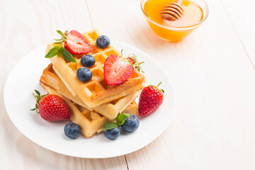 Fresh homemade food of berry Belgian waffles with honey, chocolate, strawberry, blueberry, maple syrup and cream. Healthy dessert breakfast concept with juice