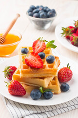 Fresh homemade food of berry Belgian waffles with honey, chocolate, strawberry, blueberry, maple syrup and cream. Healthy dessert breakfast concept with juice
