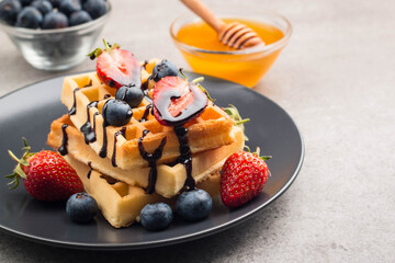 Fresh homemade food of berry Belgian waffles with honey, chocolate, strawberry, blueberry, maple syrup and cream. Healthy dessert breakfast concept with juice